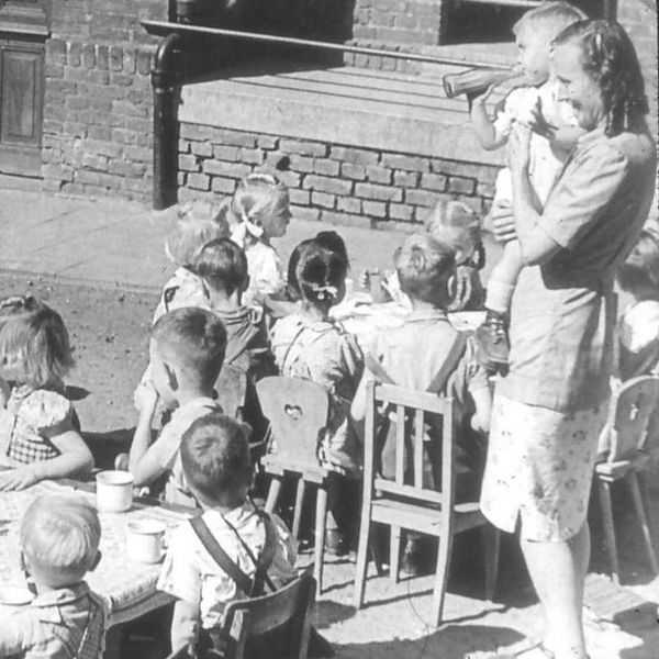 Ein altes Schwarz-weiß-Bild von einer Gruppe Kinder mit einer Erzieherin.