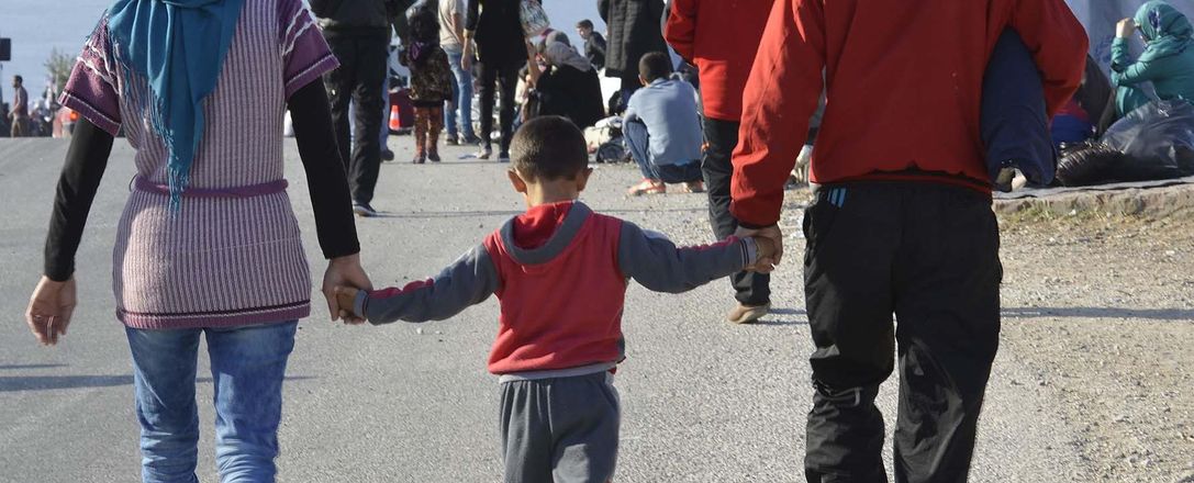 Zwei Erwachsene laufen mit einem Kind in ihrer Mitte an den Händen durch ein Flüchtlingslager