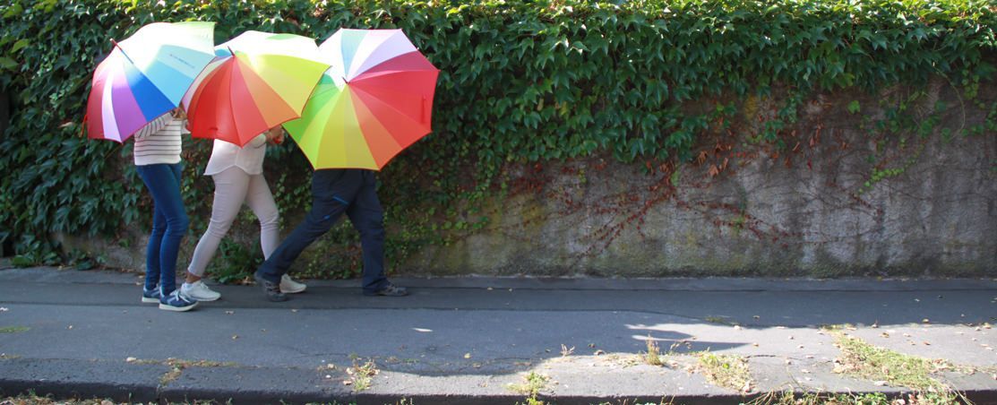 Drei Menschen mit bunten Regenschirmen